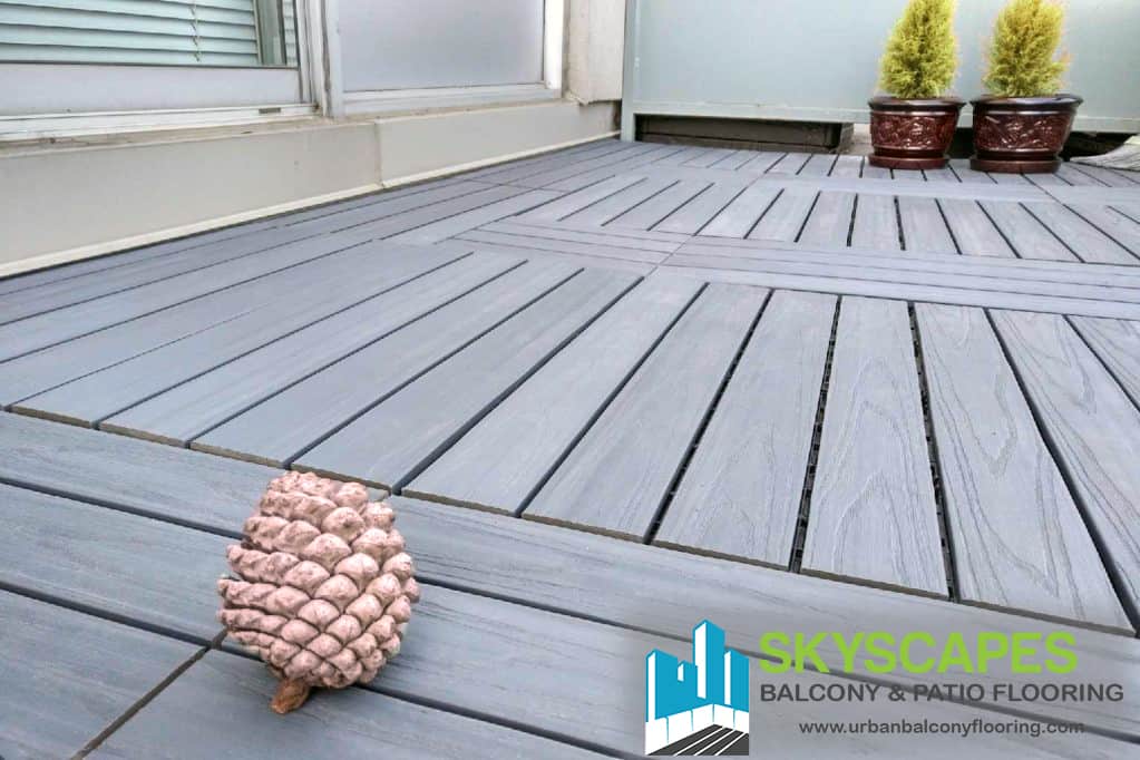 Grey, 4-slat 2x1 foot WPC tiles on balcony floor. Skyscapes green and blue logo at bottom-right of image.