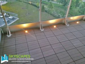 Teak Composite Tiles and Lights on Toronto Balcony. Ridged WPC Tile seen on balcony floor. Measures 1 by 1 feet. Skyscapes green and blue logo at bottom-left of image.