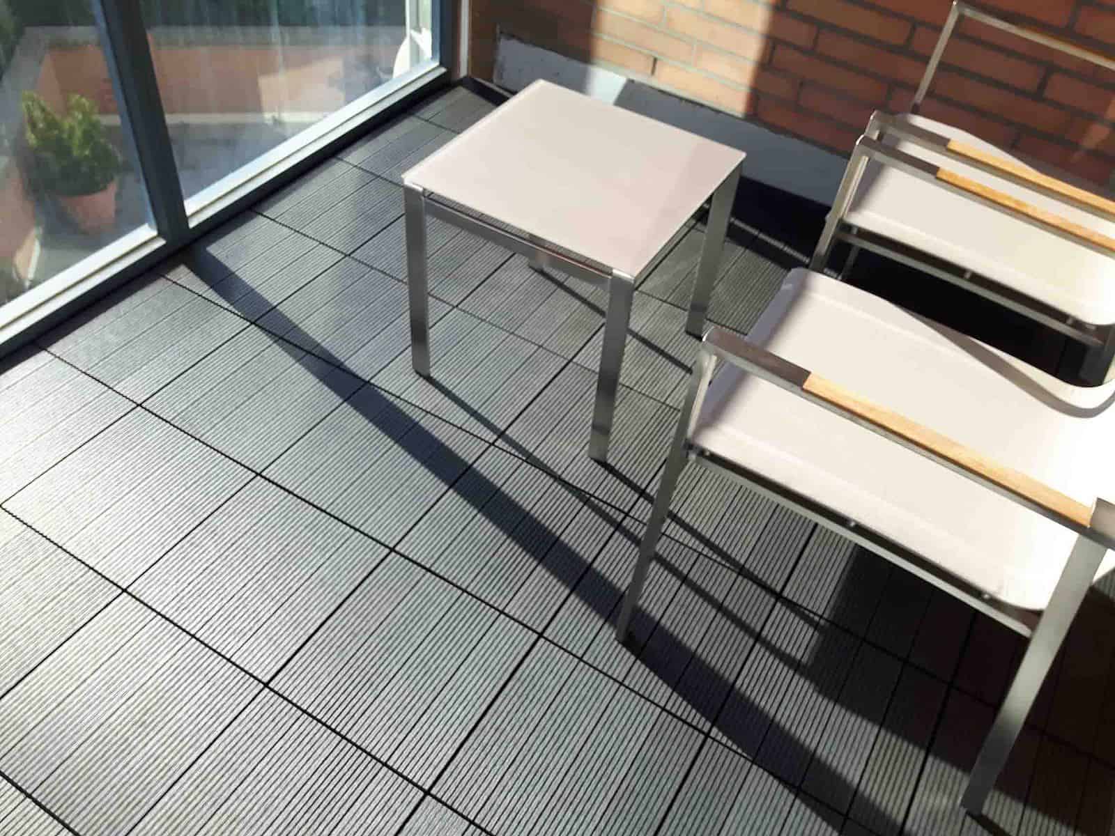 Charcoal, 4-slat, ridged WPC Tile seen on balcony floor with nice modern furniture. Measures 1 by 1 feet.