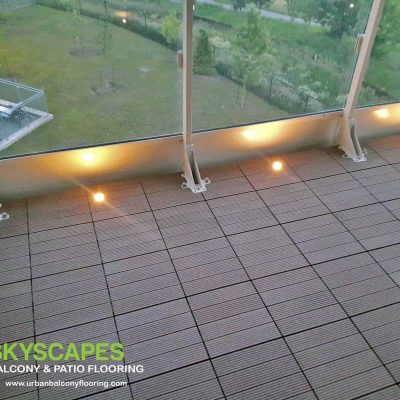 Teak Composite Tiles and Lights on Toronto Balcony. Ridged WPC Tile seen on balcony floor. Measures 1 by 1 feet. Skyscapes green and blue logo at bottom-left of image.